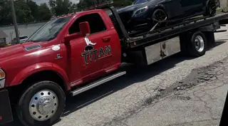 Titan red rollback flatbed with a car loaded on the deck.