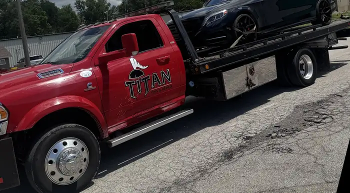Titan red rollback flatbed with a car loaded on the deck.